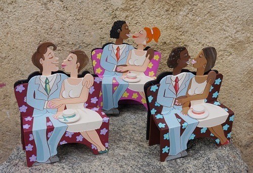 Illustration of three couples in wedding attire sitting on benches, each pair consisting of a bride and groom of varying skin tones, set against a textured outdoor backdrop reminiscent of scenic views found on cycling tours.