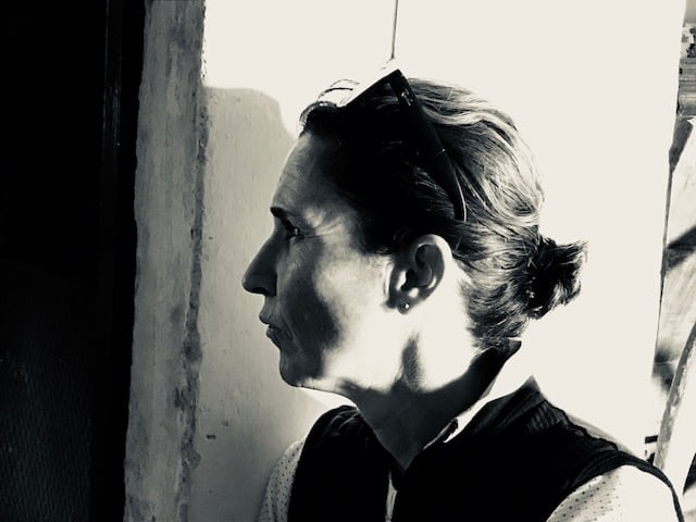 Black and white photo of a woman with hair pulled back, glasses on her head, looking left in profile, standing near a sunlit wall—capturing the thoughtful spirit perfect for scenic bike tours.