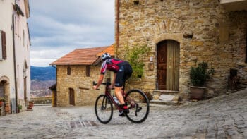 Vibrant cyclist riding through an Italian village cobblestone street, showcasing scenic Italy bike tours with picturesque historic architecture.