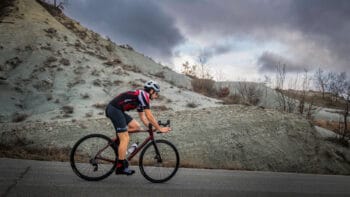 Bike rider on a scenic Italy cycling tour along a mountainous road during cloudy weather.
