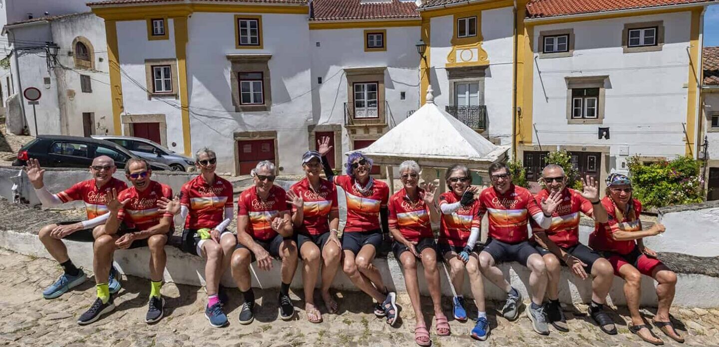 Group of cyclists wearing matching red jerseys resting on a stone bench in a scenic Italian village, enjoying Italy bike tours with Ciclismo Classico.