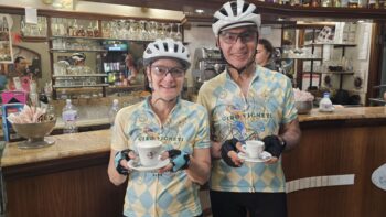 Enjoying a coffee break at a cozy Italian café during a scenic Italy bike tour, featuring smiling cyclists in cycling jerseys and helmets.