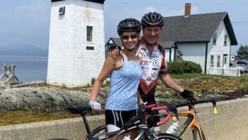 Biking couple enjoying Italy bike tour by lighthouse and charming coastal village features scenic scenery and cycling adventure, perfect for outdoor enthusiasts seeking the best bike tours in Italy.