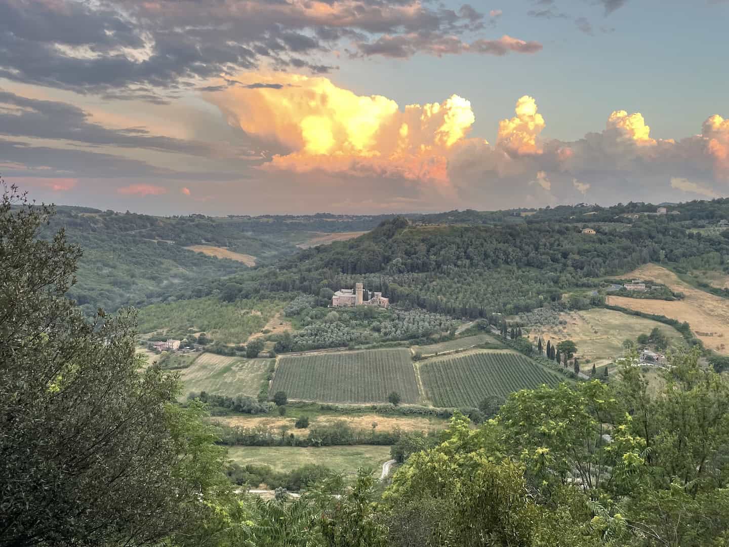 Rolling hills with vineyards and a historic castle in Tuscany during sunset, showcasing Italy's scenic bike tour routes and picturesque landscapes.