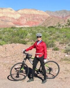 Biker in red jacket and helmet standing with a mountain bike at colorful canyon in Italy during an outdoor cycling tour.