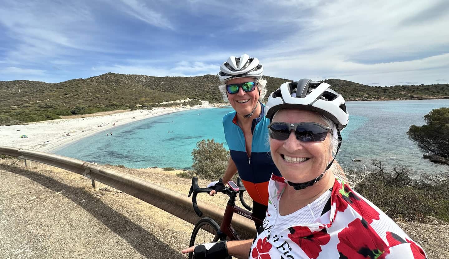 A sunny day cycling tour along a scenic Italian coastline with smiling women in helmets and sunglasses, enjoying the picturesque views of turquoise waters and lush hills.