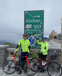 Gorgeous mountain climbers posing with their bikes at a scenic Italian viewpoint on a cloudy day.
