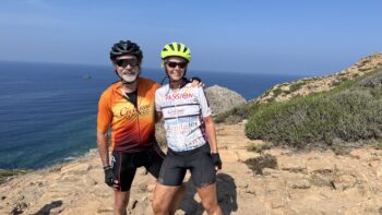 Biking photo of smiling cyclists enjoying a scenic coastal ride along Italy's cliffs with the sea in the background.