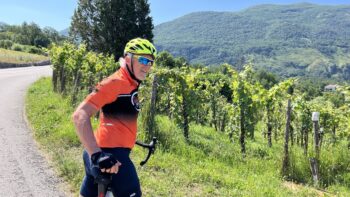 Scenic Italy bike tour with cyclist enjoying lush vineyard landscape and mountain views in Italy.