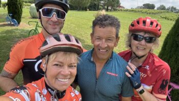 A group of four cyclists enjoying Italy bike tours in a lush, green countryside with colorful bicycles and scenic vineyards in the background.