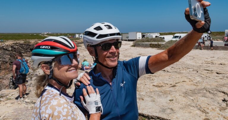 Two cyclists wearing helmets and sunglasses taking a selfie during an Italy bike tour, enjoying scenic outdoor views and memorable moments on a sunny day.