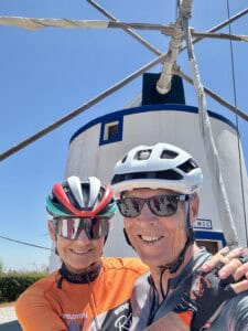 Vibrant Italian bike tour with cyclists in front of a historic windmill on a sunny day, showcasing Italy's scenic cycling routes.