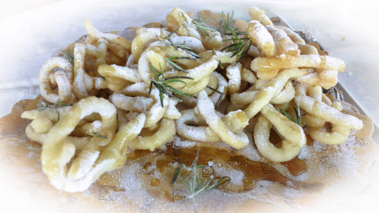 Crispy fried gelato fritters with powdered sugar and fresh herbs on a white surface.