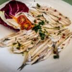 Fresh Italian sardines with herbs and cherry tomatoes served on a white plate, highlighting Italy's rich seafood cuisine.