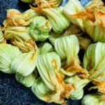 Fresh zucchini blossoms on a dark countertop, showcasing vibrant green and orange colors, ideal for authentic Italy cuisine and bike tours in Italy.