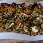 Grilled eggplant and zucchini drizzled with balsamic glaze and garnished with fresh herbs on a white platter.