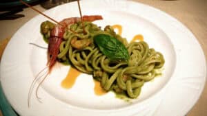 Fresh Italian seafood pasta dish with prawns, basil, and green sauce served on a white plate in Italy.