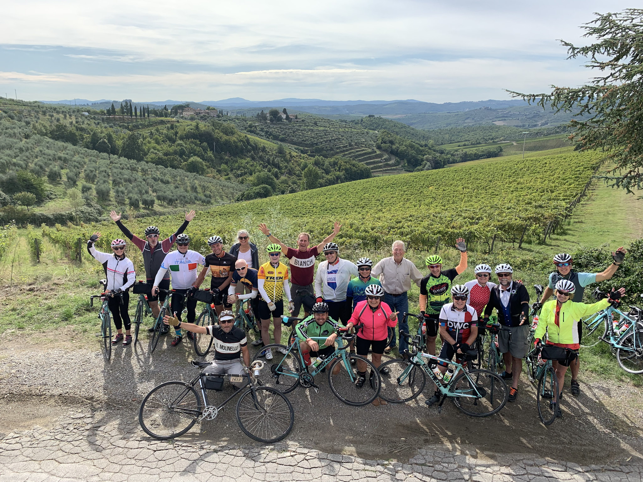 Vibrant group of cyclists enjoying scenic Italy bike tour through lush vineyards and rolling hills in Tuscany, surrounded by picturesque landscapes on a sunny day.