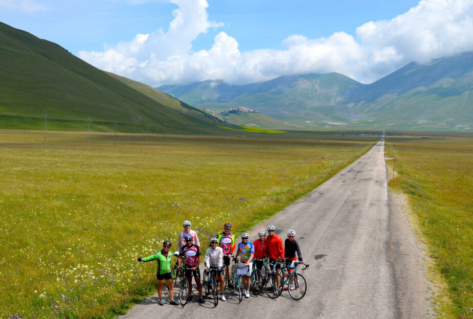 Cycling group on a scenic Italy bike tour through lush green fields and rolling mountains, ideal for adventure and exploring the best biking routes in Italy.