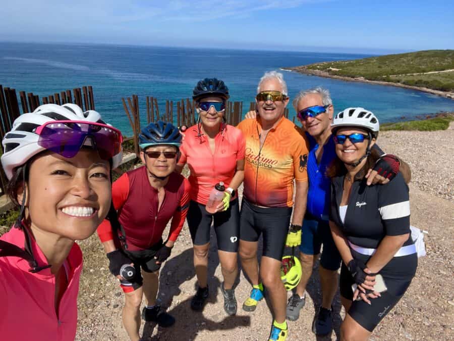 Enjoying a scenic Italy bike tour along the coast with a group of cyclists in colorful gear, overlooking the blue sea and rugged shoreline.
