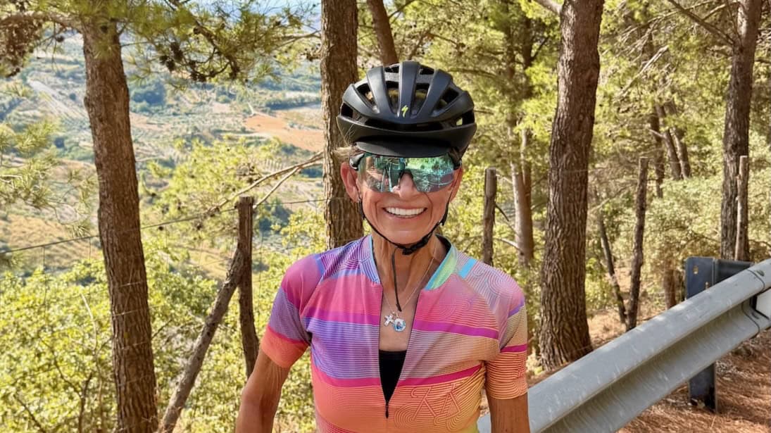 A smiling female cyclist wearing a helmet and sunglasses enjoying a scenic bike ride through a forested area in Italy, highlighting the beauty of Italy bike tours and outdoor cycling adventures.