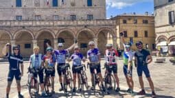 Group of cyclists in colorful gear standing with bikes in a historic Italian town square, showcasing scenic bike tours in Italy for cycling enthusiasts.
