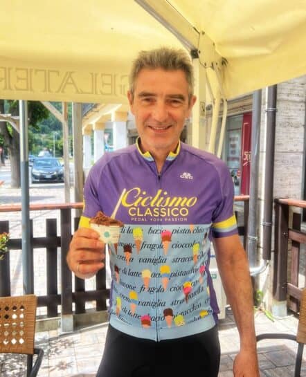 Smiling cyclist in Italy holding a gelato, promoting bike tours in Italy with Ciclismo Classico, a top bike tour company in Italy.