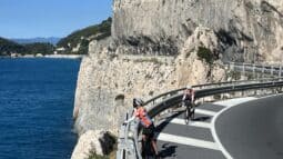 Cyclists riding along a scenic coastal road in Italy with cliffs and blue sea in the background, showcasing Italy bike tours and scenic cycling routes.