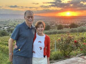 Elderly couple smiling during a bike tour in Italy at sunset, with scenic vineyards and rolling hills in the background, highlighting Italy bike tours and cycling experiences.